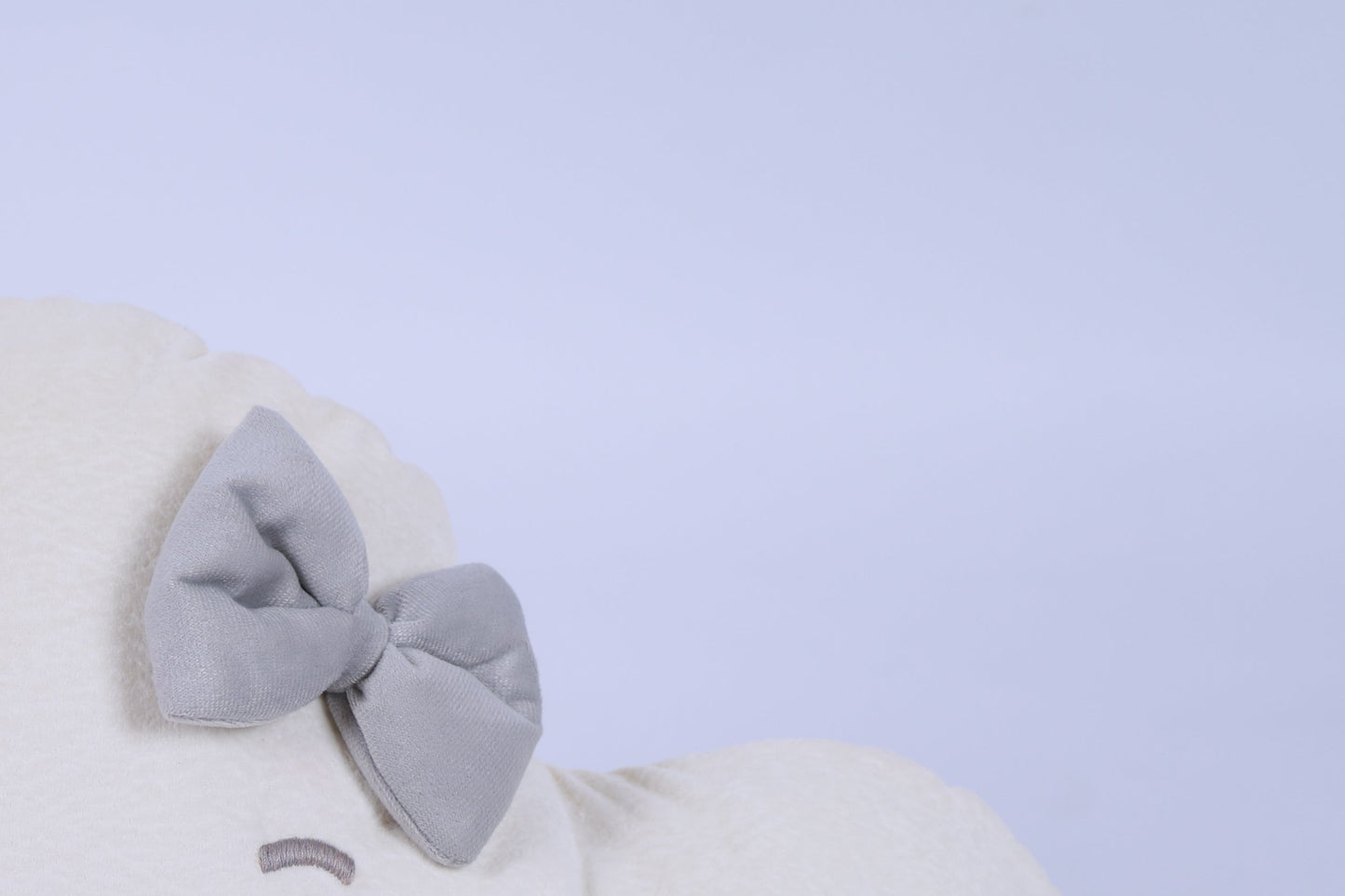 White plush toy with a large gray bow on a light blue background