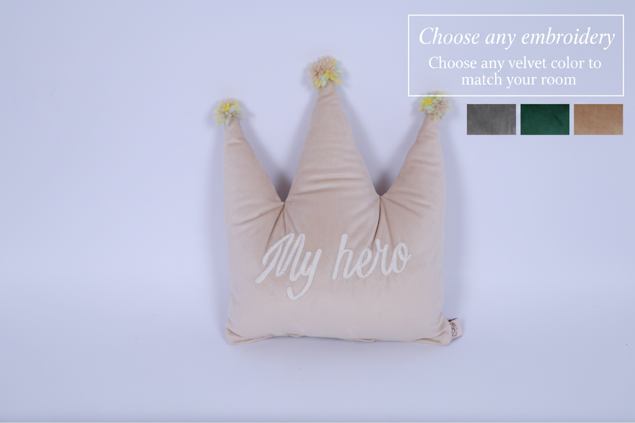 Beige crown-shaped pillow with 'My hero' text on a light purple background