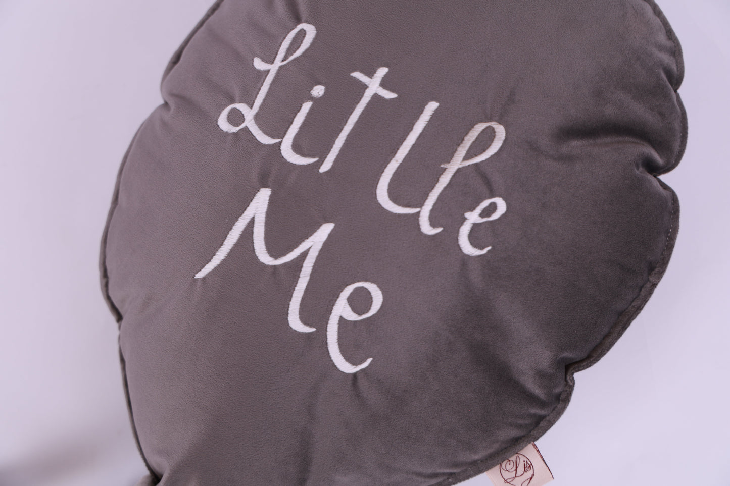 Round gray pillow with 'Little Me' text on a light purple background