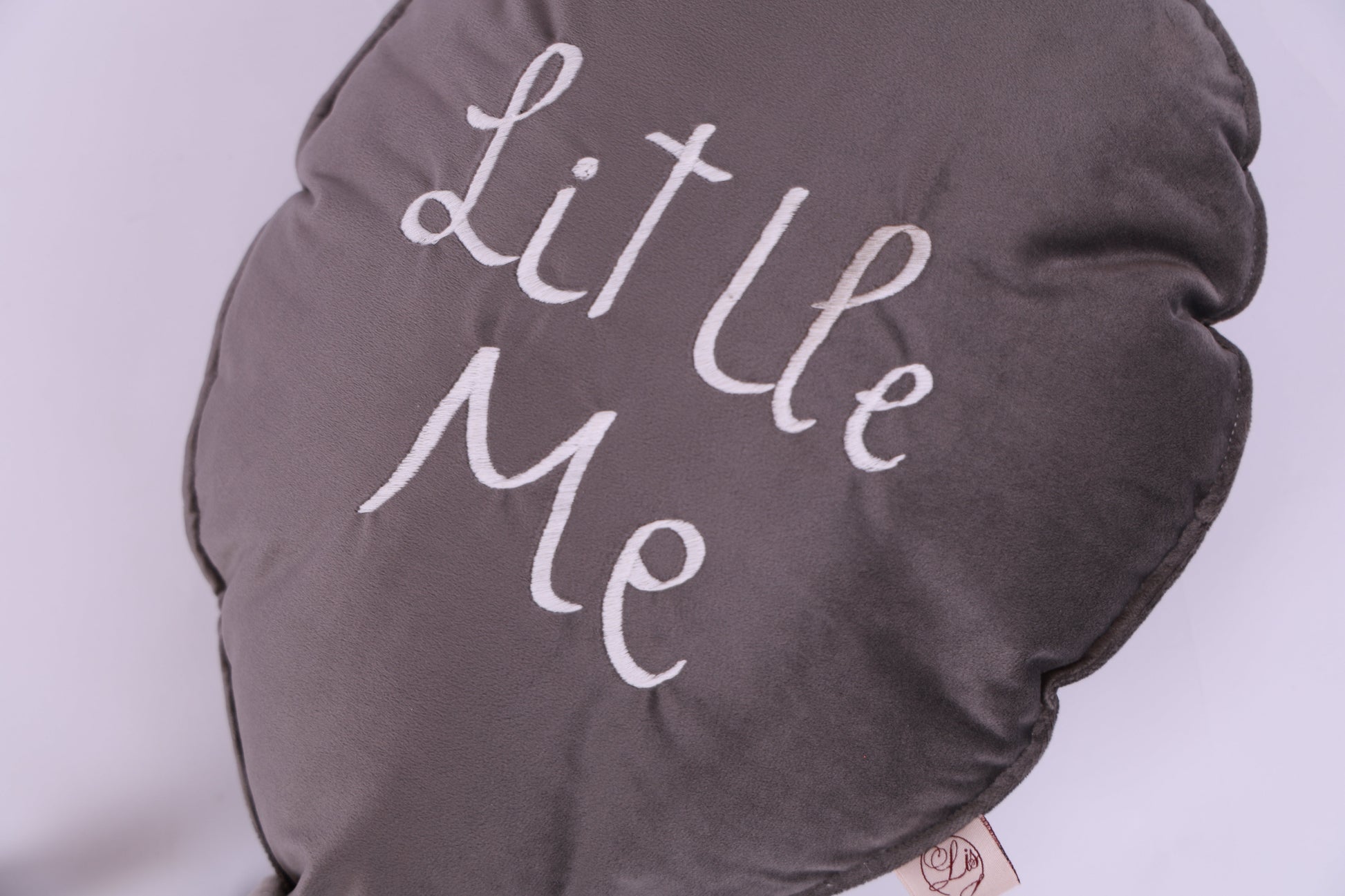 Round gray pillow with 'Little Me' text on a light purple background