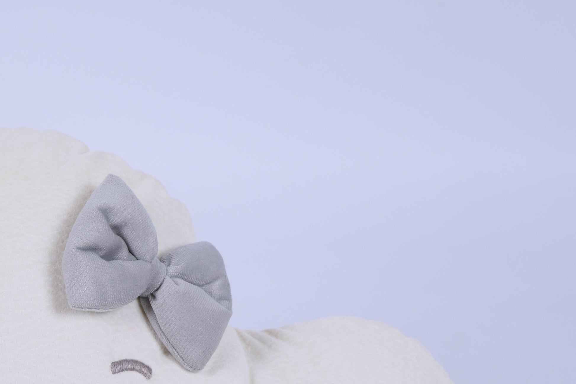 White plush toy with a large gray bow on a light blue background