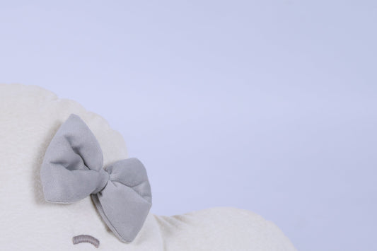 White plush toy with a large gray bow on a light blue background